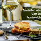 Geröstete Brioche-Scheiben mit Aufstrich auf Schieferplatte, dazu ein Glas Weißwein; Text: Genießen wie Gott in Frankreich